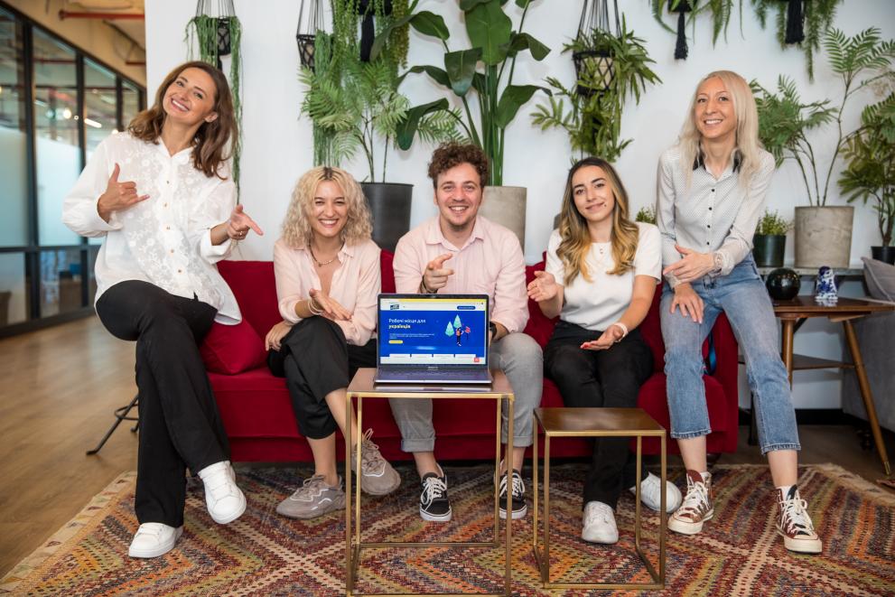 5 young professionals smiling for the camera in front of a computer